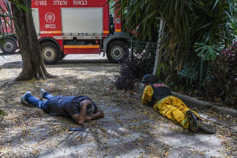 رجل إطفاء إسرائيلي ومدني على الأرض بينما تنطلق صفارات الإنذار تحذيراً من الصواريخ الآتية من لبنان (رويترز)
