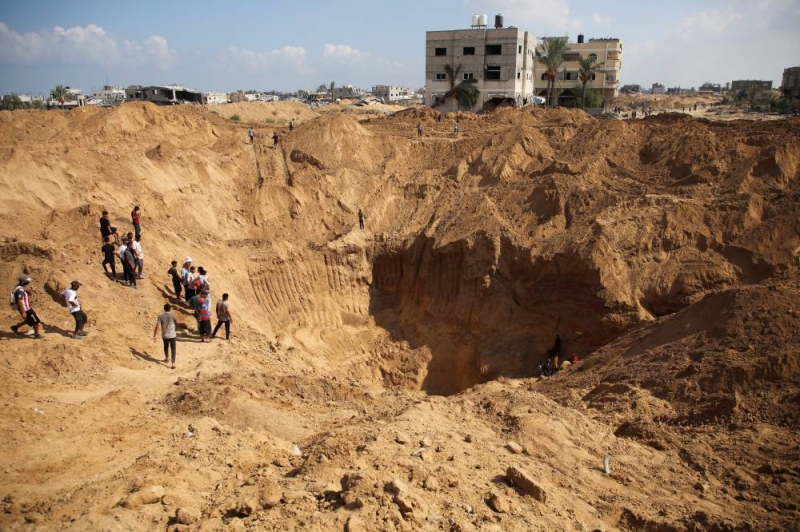 فلسطينيون قرب حفرة ضخمة جراء تنقيب الاحتلال عن أنفاق في غزة (رويترز)